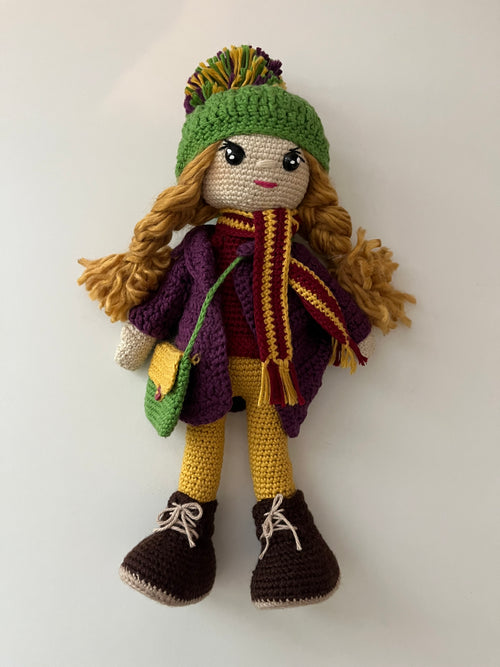 Handmade crochet doll with green hat and purple and yellow outfit on a white background