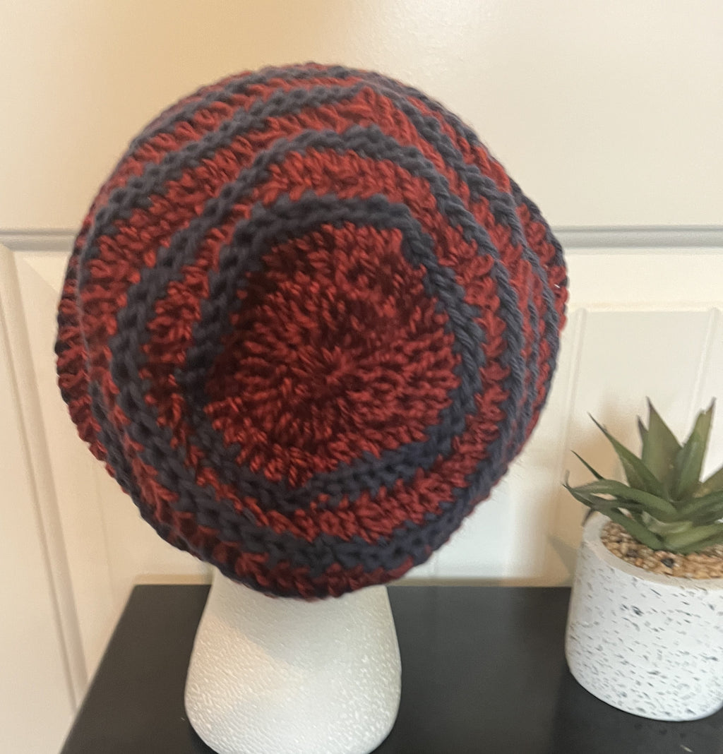 Knitted beanie in red and black on a mannequin head with a plant in the background