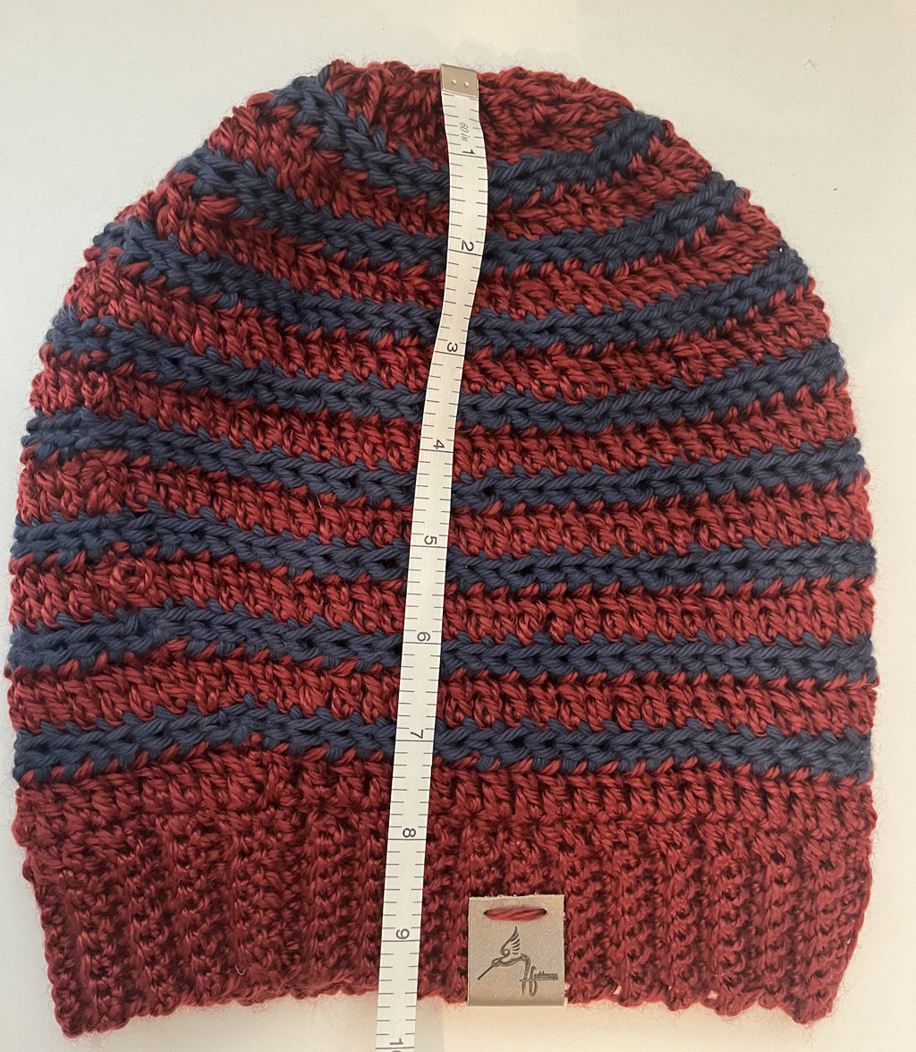 Red and blue striped knitted beanie with a measuring tape and brand label on a white background