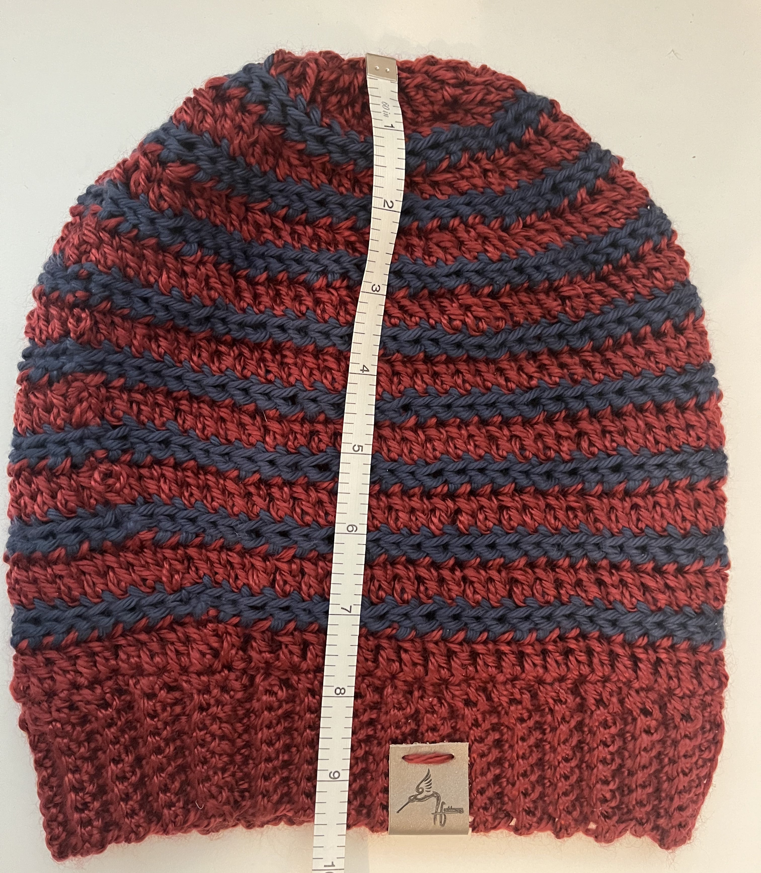 Red and blue striped knitted beanie with a measuring tape and brand label on a white background