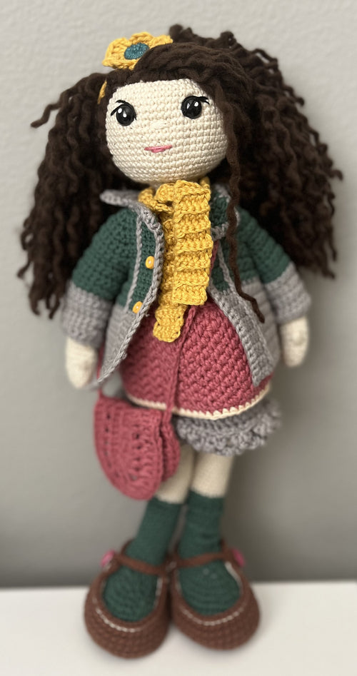 Crocheted doll with brown hair, yellow headband, and colorful outfit on a plain background